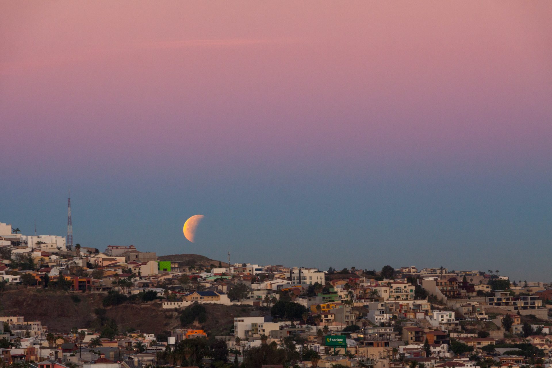 Moonrise over a coastal city at dusk