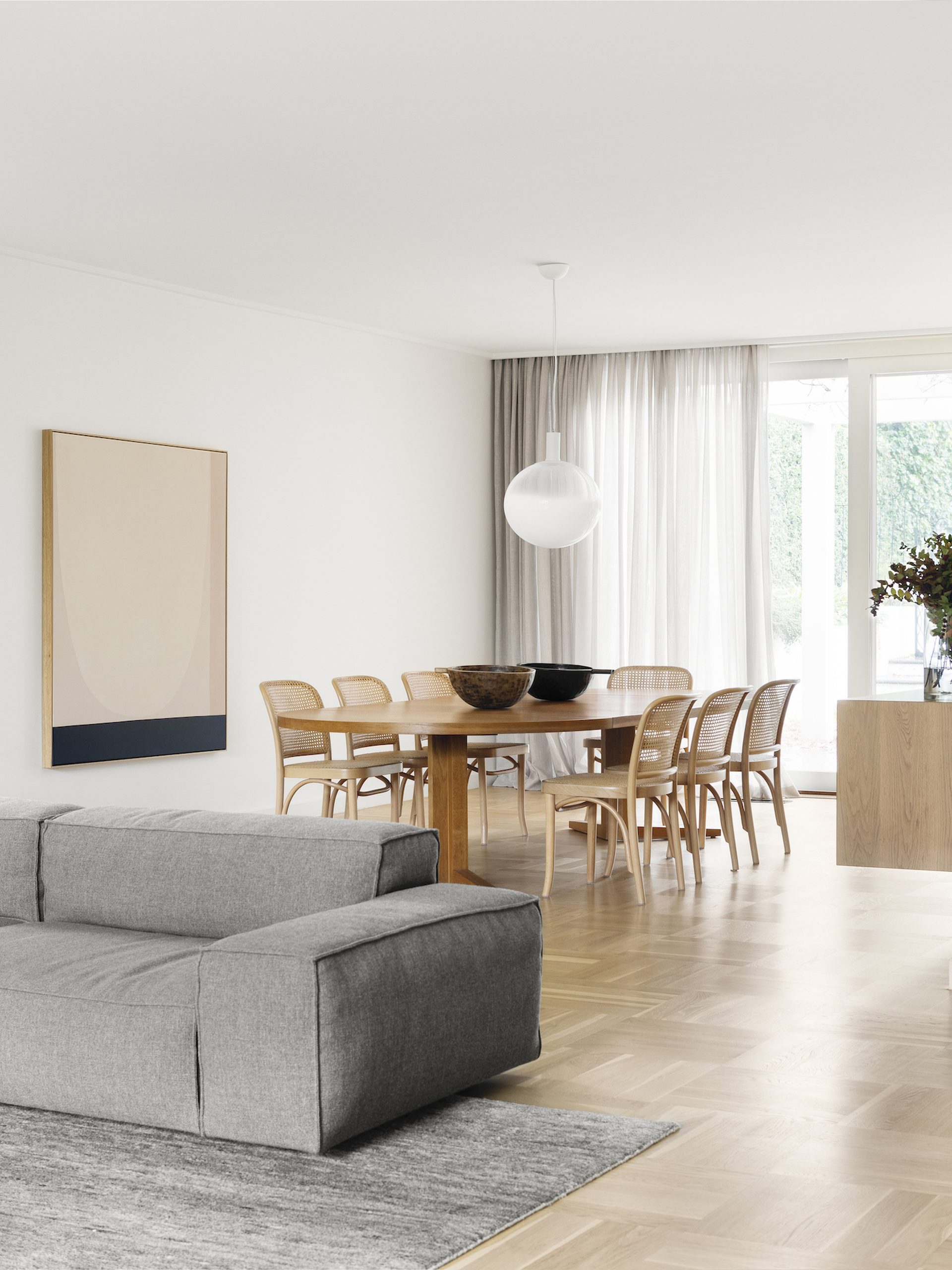 Bright dining room with rattan chairs and a grey sofa